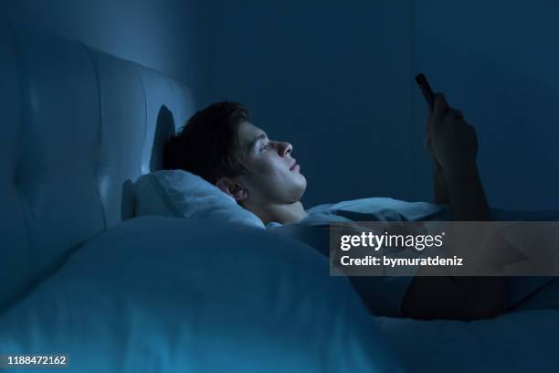 müde und gestresst auf dem bett in der nacht - bed phone stock-fotos und bilder