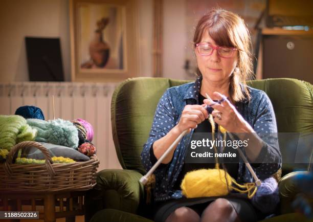 mid age frau sitzen und stricken einen artikel in gelber wolle - knitting stock-fotos und bilder