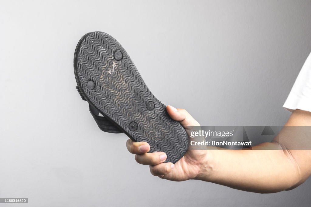 Hand holding old and dirty sandal as a weapon for killing an insect