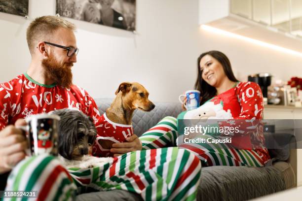 couple wearing christmas pajamas with dogs on sofa - ugly dog stock pictures, royalty-free photos & images