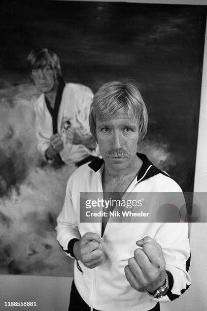 Martial arts action movie star Chuck Norris poses infant of action poster on the wall of his home in Palos Verdes Southern bcaliforia circa 1978 .