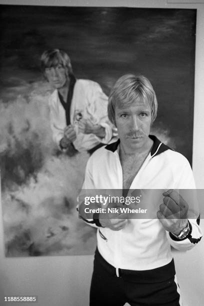 Martial arts action movie star Chuck Norris poses infant of action poster on the wall of his home in Palos Verdes Southern bcaliforia circa 1978 .
