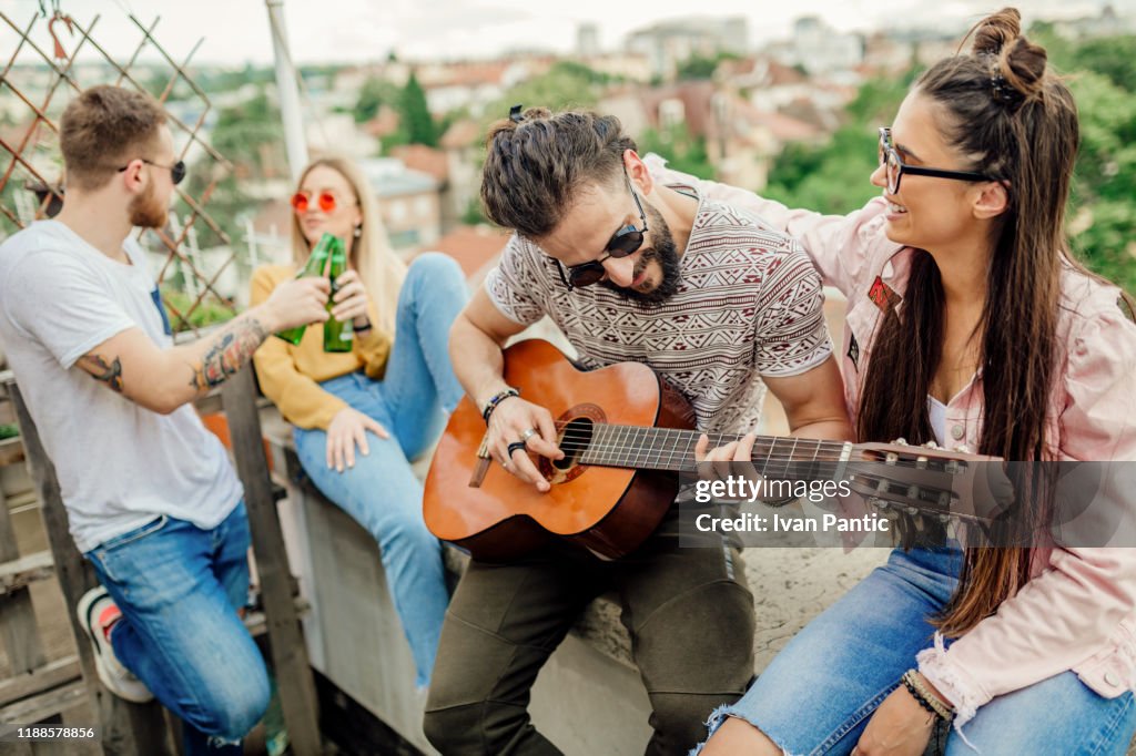 Young men and women sitting on top of the roof, having fun