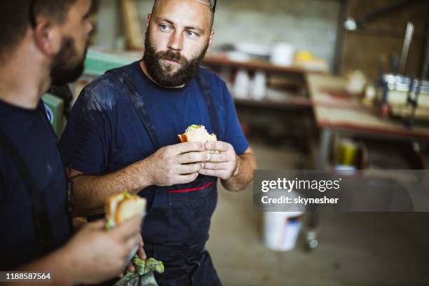 jonge arbeiders praten terwijl ze broodjes eten tijdens een pauze in een workshop. - lunchpauze stockfoto's en -beelden