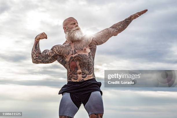 tattooed senior man during beach workout - muscle men at beach stock pictures, royalty-free photos & images