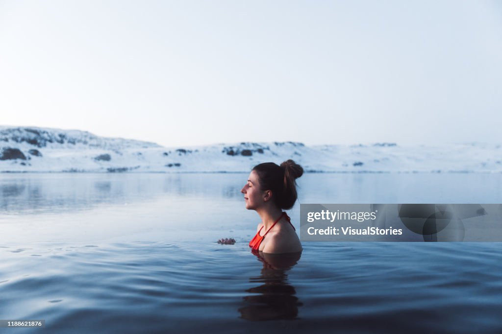 Donna che nuota nella piscina termale con vista sulle splendide montagne innevate in Islanda