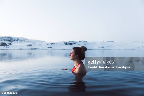 kvinna som simmar vid termalpoolen med utsikt över vackra snötäckta berg på island - winter bildbanksfoton och bilder