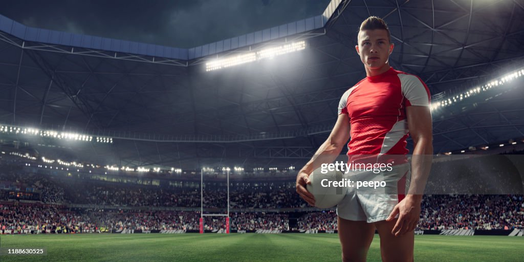 Rugby Player Standing With Ball In Floodlit Stadium Before Match
