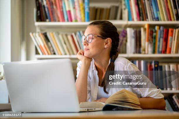 deconcentrated young adult woman looking away while studying in library - adhs stock pictures, royalty-free photos & images
