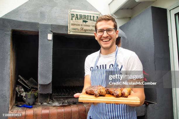 millennial argentinian cook presenting roasted rib eye and strip steaks - argentinian ethnicity stock pictures, royalty-free photos & images