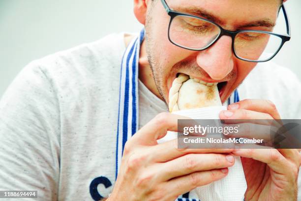 primer plano sobre el joven mordiendo en una empanada tucumana envuelta en papel - empanadas fotografías e imágenes de stock