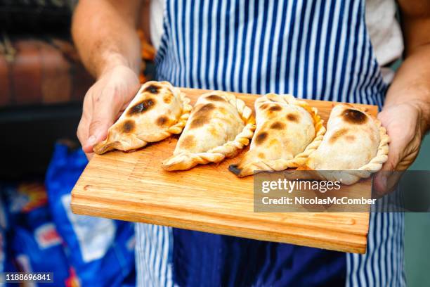 primer plano de empanadas perfectamente horneadas tucumanas en una tabla de cortar sostenida por panadero - argentina fotografías e imágenes de stock