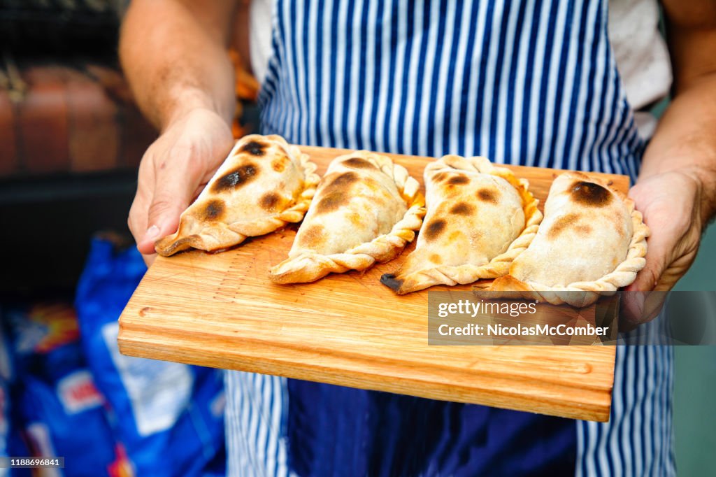 Close-up em tucumanas perfeitamente cozidos das empanadas em uma placa de corte prendida pelo padeiro