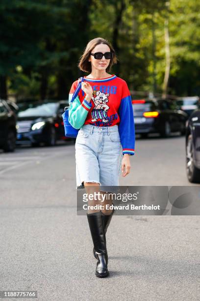 Mary Leest wears sunglasses, a blue Tod's bag, a red knit sweater with a comics picture pattern and green and blue mismatched sleeves, a blue denim...