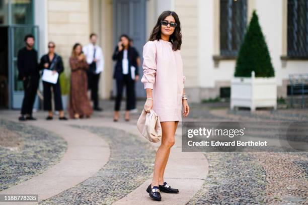 Paola Alberdi wears sunglasses, a light pink leather long sleeves mini dress, a beige puff clutch, black moccasins with a metallic strap, outside the...