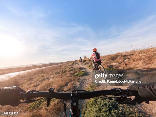 pov, family riding mountain bikes le long du sentier shoreline à voie unique - rive photos et images de collection