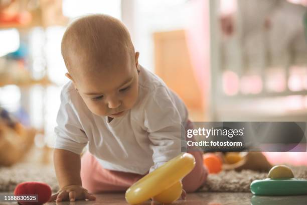 baby girl crawling on the living room and looking at toy - baby on the move stock pictures, royalty-free photos & images