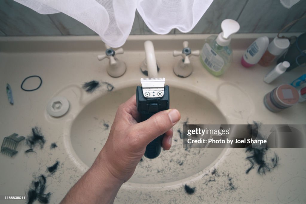 Man holding electric shaver with hair all over sink