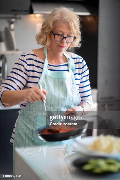 senior woman stirring tomato sauce - stir frying european stock pictures, royalty-free photos & images