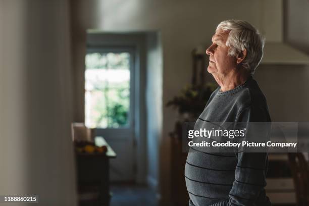 sad senior man kijkt uit door een raam thuis - mourner stockfoto's en -beelden