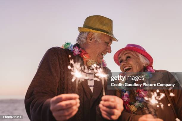 aînés riants célébrant le nouvel an avec des cierges à la plage - couple de vieux drole photos et images de collection
