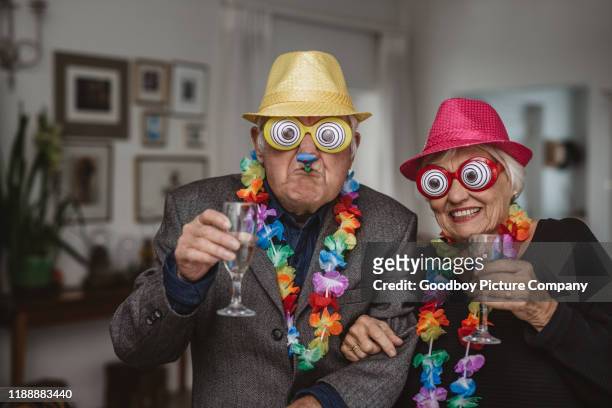senior-paar trinken und tragen neuheit brille auf einer party - kostüm stock-fotos und bilder