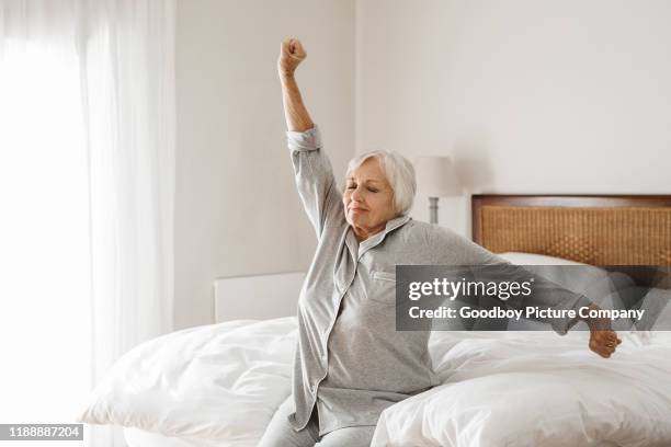 lachende senior vrouw die zich uitstrekt op haar bed in de ochtend - yawning woman stockfoto's en -beelden