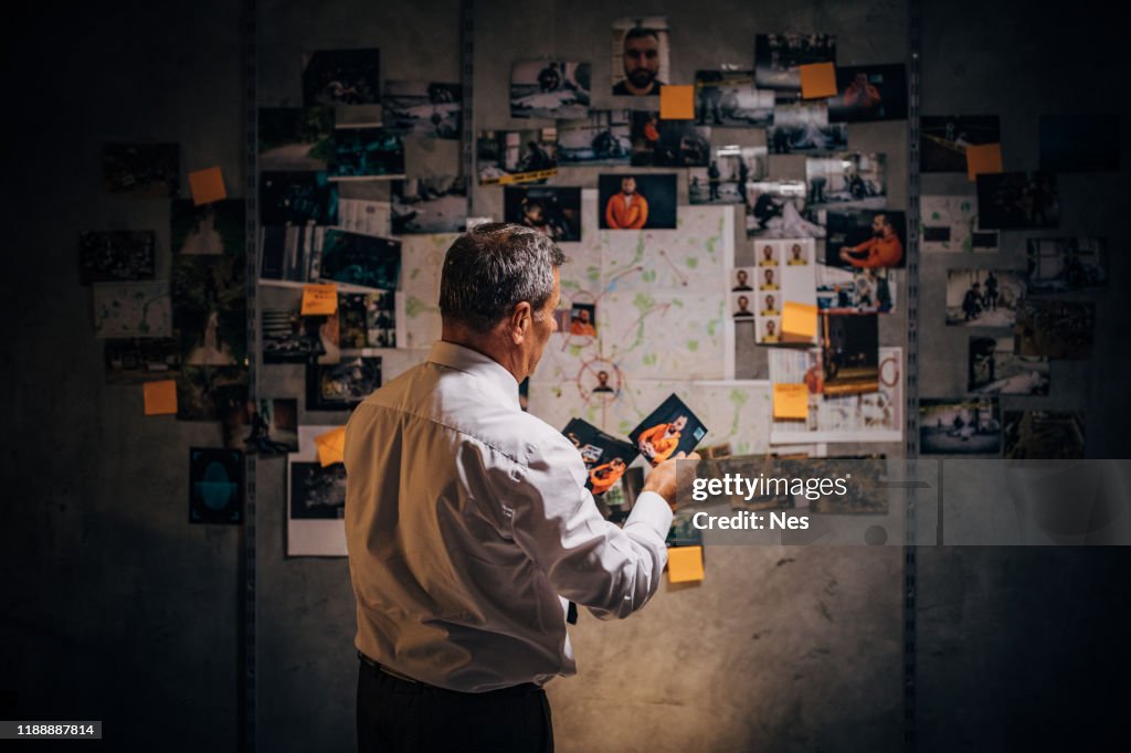 Ein alter Detektiv schaut sich Fotos von Verdächtigen in seinem Büro an
