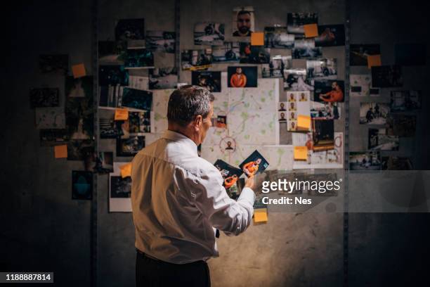 un vecchio detective sta guardando le foto dei sospetti nel suo ufficio - investigatore foto e immagini stock