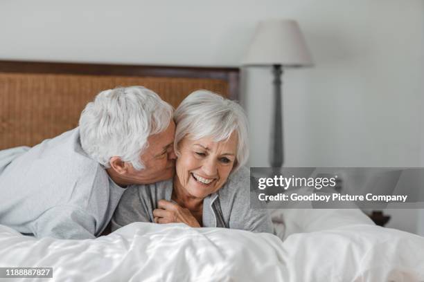 homem sênior afectuoso que beija sua esposa de sorriso na cama - couple and kiss and bedroom - fotografias e filmes do acervo