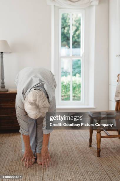 mujer mayor haciendo estiramientos después de despertarse por la mañana - tocar los dedos de los pies fotografías e imágenes de stock