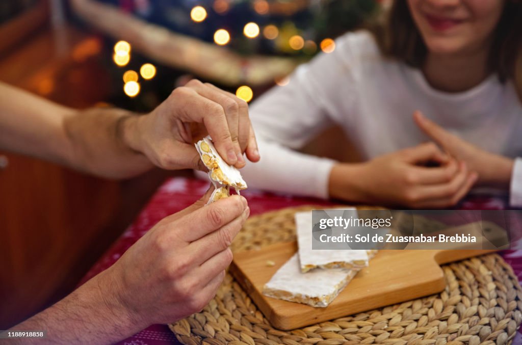 Father and daughter sharing time at Christmas, eating almond nougat next to the Christmas tree
