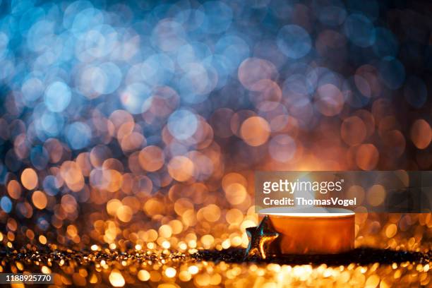 geleuchtete kerze auf defokussiertem blauem hintergrund - christmas tea light - advent stock-fotos und bilder