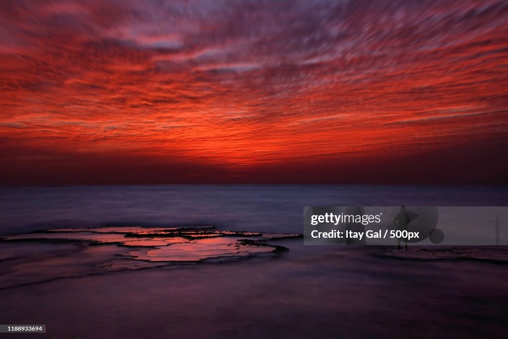 Silhouette of lone man fishing in sea at sunset