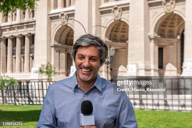 male mature reporter talking and holding a microphone in a public park during a sunny day at buenos aires, argentina. - holding microphone stock pictures, royalty-free photos & images