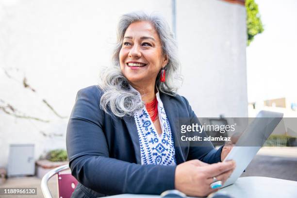 latina businesswoman using tablet at cafe - baby boomer stock pictures, royalty-free photos & images