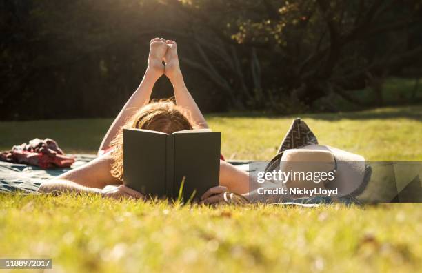 perdido en su libro favorito - mujer leyendo libro en el parque fotografías e imágenes de stock