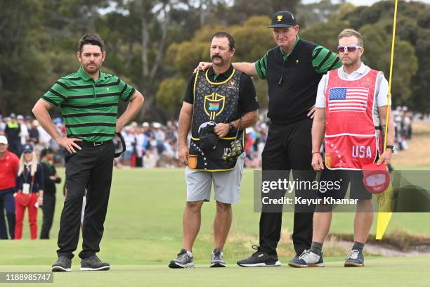 International team captain, Ernie Els, hugs Louis Oosthuizen's caddie Wynand Stander as Matt Kuchar's caddie, John Wood watches during the final...