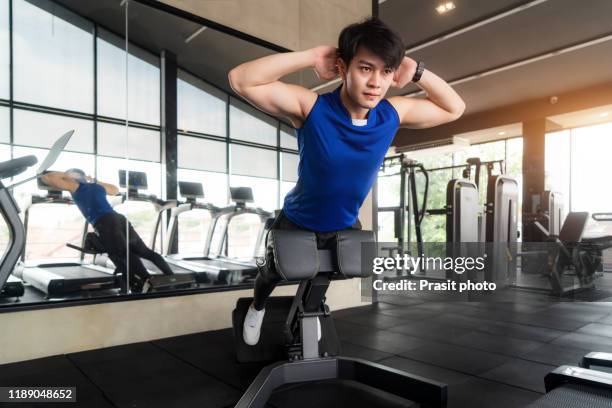 portrait of handsome asian man wearing blue sportswear working out on back muscles machine at the gym. fitness, sport, training, gym and lifestyle concept - hamstring machine stock pictures, royalty-free photos & images