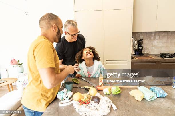 Cheerful girl with dads playing with cucumber on her eyes