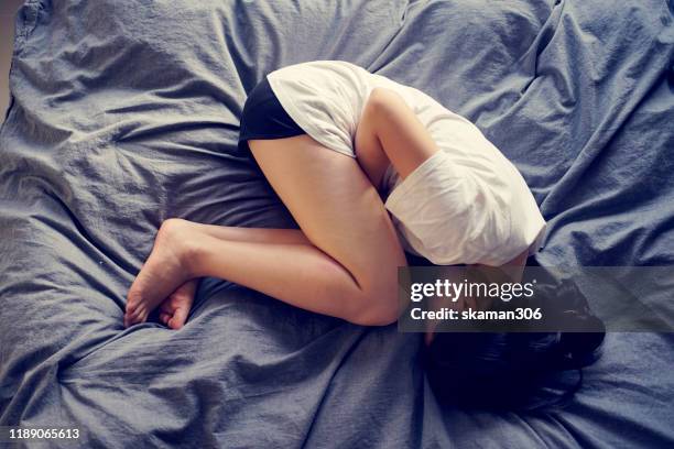 asian female feel hurt and pain on period on the bed - stili foto e immagini stock