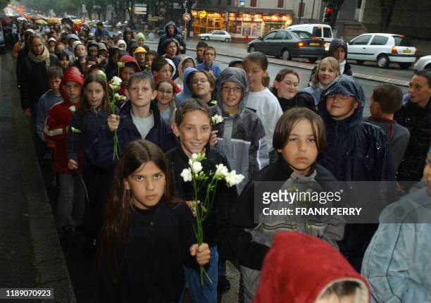 Environ 2.500 écoliers, collégiens et lycéens, ainsi qu'un demi-millier d'adultes, patientent pour déposer une fleur blanche sur un drapeau...