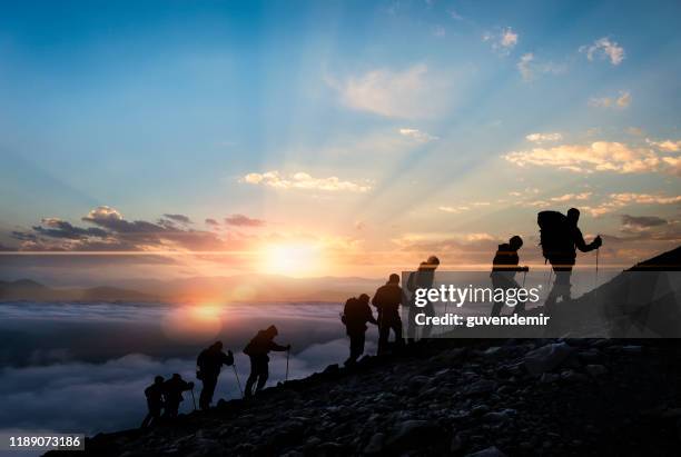 silhouetten von wanderer bei sonnenuntergang - bergsteiger gipfel stock-fotos und bilder