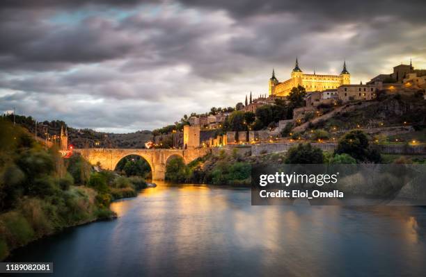 alcazar and alcantara bridge in toledo at sunset reflected in tajo river - toledo province stock pictures, royalty-free photos & images