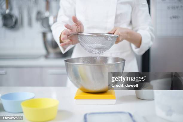 young asian woman sifting flour in a mixing bowl - sifting stock photos et images de collection