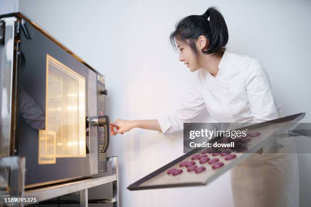 young asian woman baker with oven - macaroons stockfoto's en -beelden