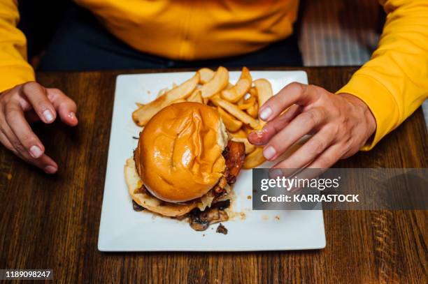 close up of a male hands holding hamburger. other food in the background. only daylight used. - male burger eating fotografías e imágenes de stock