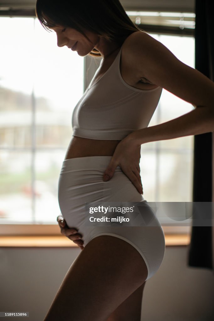 Pregnant woman in bedroom touching her abdomen