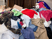 Large messy pile of household items, clothes, boxes, hangers, bubble wrap, toilet paper, pants, shirts, dresses with curtains and mirror in background