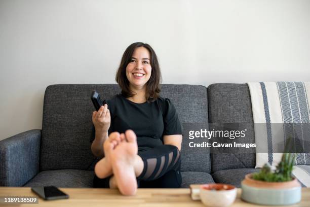 woman sitting on couch with feet up holding remote - american pie movie fotografías e imágenes de stock